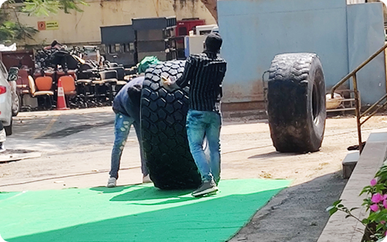 Two guys are rolling a big tyre around.